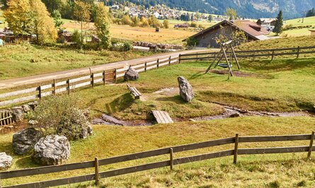 Ländliche Szene mit Holzzaun, Spielplatz, Bachlauf und Bergen im Hintergrund