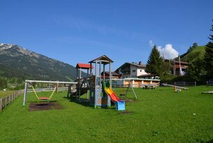 Spielplatz mit Rutsche, Schaukel und Wippe vor Bergkulisse