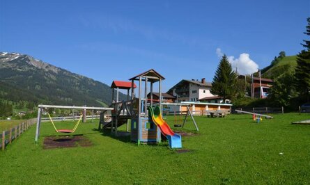 Spielplatz mit Rutsche, Schaukel und Wippe vor Bergkulisse
