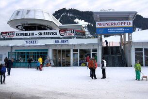 Skigebäude mit Skiverleih und Ticketverkauf im Schnee, Menschen davor, Berg im Hintergrund