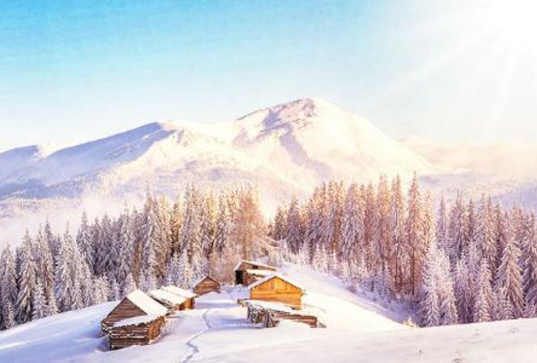 Verschneite Holzhütten vor schneebedecktem Berg und Wald im Winter
