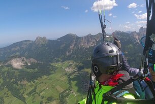 Gleitschirmflieger vor Berglandschaft mit grünen Wiesen und blauem Himmel