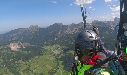 Gleitschirmflieger vor Berglandschaft mit grünen Wiesen und blauem Himmel