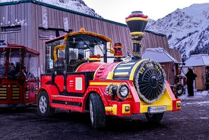 Rote, festlich geschmückte Bimmelbahn mit Rädern vor verschneiter Bergkulisse