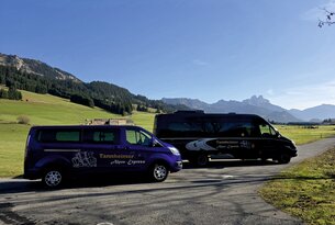 Zwei Kleinbusse mit Aufschrift Tannheimer Alpen Express vor Berglandschaft
