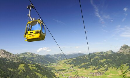 Gelbe Gondelbahn über grüner Berglandschaft mit Häusern unter blauem Himmel