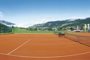 Tennisplatz mit rotem Sand vor Berglandschaft unter blauem Himmel