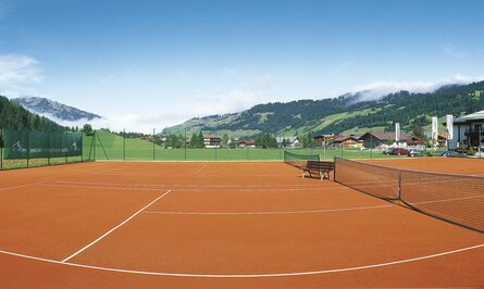 Tennisplatz mit rotem Sand vor Berglandschaft unter blauem Himmel