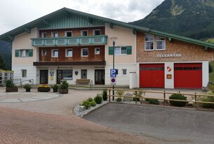 Dorfgebäude mit Feuerwehrhaus und Bankfiliale vor Bergkulisse