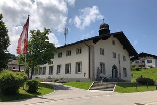 Gemeindehaus mit Schweizer Flagge vor blauem Himmel mit Wolken