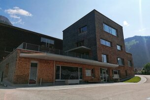 Modernes Gebäude mit dunklem Anbau und hellerer Fassade unter blauem Himmel