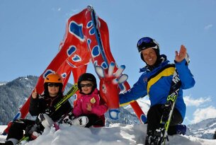 Familie mit Skiausrüstung posiert vor roter Giraffenstatue im Schnee