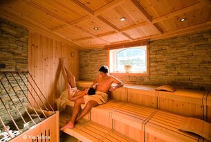 Paar sitzt entspannt in einer hellen Holzsauna mit Fenster