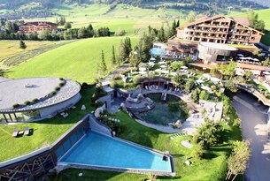 Hotelanlage mit Pools, Liegen und Grünflächen vor Bergkulisse