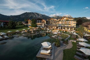 Hotelanlage mit See und Liegen vor Bergkulisse