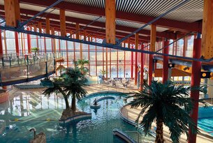 Hallenbad mit Palmen, Wasserrutsche und großen Fenstern