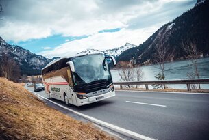 Weißer Reisebus fährt auf Straße vor Bergkulisse