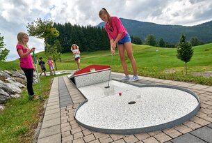 Mädchen spielt Minigolf, weitere Kinder im Hintergrund