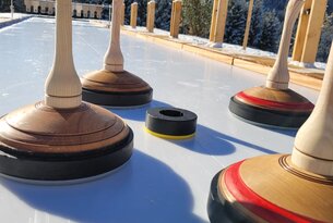 Eisstockschießen mit Eisstöcken und Daube auf Eisfläche vor verschneiter Berglandschaft
