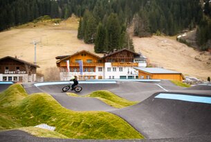 Radfahrer auf Pumptrack vor Berglandschaft mit Häusern