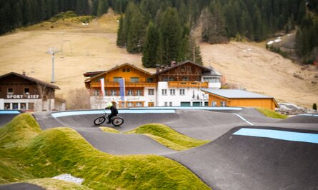 Radfahrer auf Pumptrack vor Berglandschaft mit Häusern