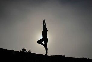 Silhouette einer Person in Yoga-Baumstellung vor hellem Hintergrund