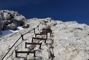 Klettersteig mit Stahlseil an steilem Felsen unter blauem Himmel