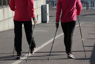 Zwei Personen beim Nordic Walking mit Stöcken auf einem Gehweg
