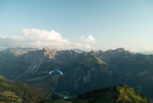 Gleitschirmflieger vor Bergpanorama unter blauem Himmel