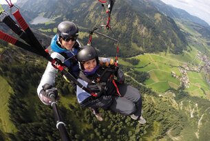Zwei Personen beim Tandem-Gleitschirmflug vor Berglandschaft