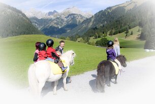 Kinder reiten auf Ponys vor Bergkulisse, begleitet von Erwachsenen