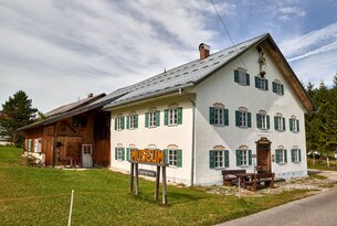 Weißes Bauernhaus mit grünen Fensterläden und Museumsschild im Garten