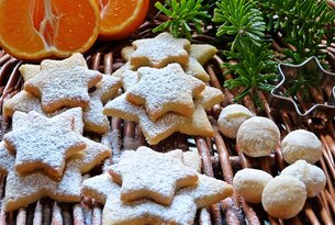 Weihnachtliches Gebäck: Sternförmige Kekse mit Puderzucker, Marzipankartoffeln, Mandarinen und Tannenzweige auf Korb
