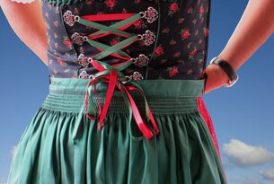Dirndl mit grüner Schürze, roter Schnürung und schwarzer Bluse mit Rosenmuster