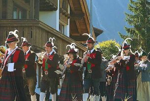 Blaskapelle in Tracht spielt vor einem Holzhaus in den Bergen