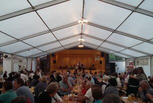 Festzelt mit Bühne, Musiker und vielen Gästen an Tischen