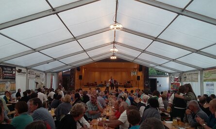 Festzelt mit Bühne, Musiker und vielen Gästen an Tischen