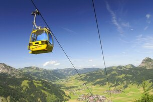 Gelbe Gondelbahn vor blauem Himmel und grüner Berglandschaft