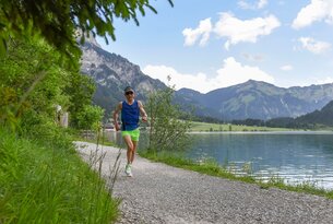 Mann joggt auf Kiesweg an See mit Bergen im Hintergrund