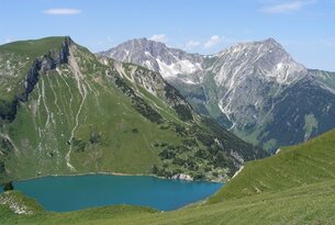 Berglandschaft mit grünem Hang und blauem See im Vordergrund