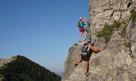 Zwei Personen klettern am Felsen mit Klettersteig-Ausrüstung