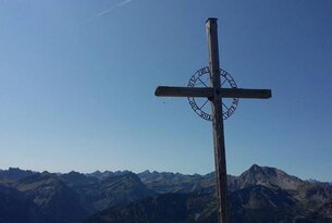 Gipfelkreuz vor Bergpanorama unter blauem Himmel