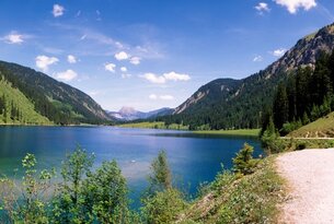 Blauer Bergsee umgeben von grünen Bergen unter blauem Himmel mit Wolken