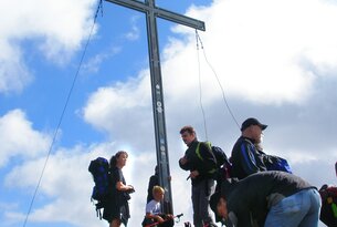 Wanderer stehen am Gipfelkreuz auf einem Berg unter blauem Himmel