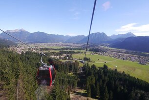 Rote Gondelbahn vor Bergpanorama und grüner Landschaft unter blauem Himmel