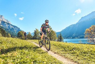 Cyclists on gravel road in front of mountain scenery and lake