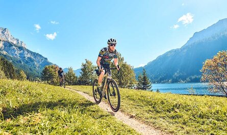 Radfahrer auf Schotterweg vor Bergkulisse und See