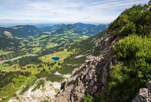Berglandschaft mit See, Wiesen und bewaldeten Hügeln unter blauem Himmel