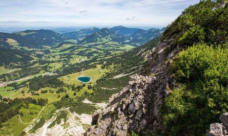 Berglandschaft mit See, Wiesen und bewaldeten Hügeln unter blauem Himmel