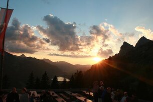 Sonnenuntergang über Berglandschaft mit See und Menschen auf Terrasse